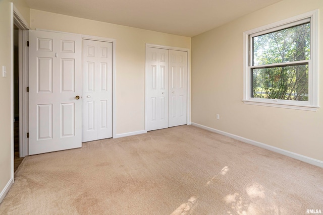 unfurnished bedroom featuring two closets and light colored carpet