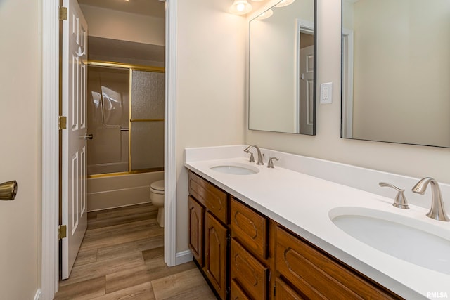 full bathroom with hardwood / wood-style floors, vanity, toilet, and bath / shower combo with glass door