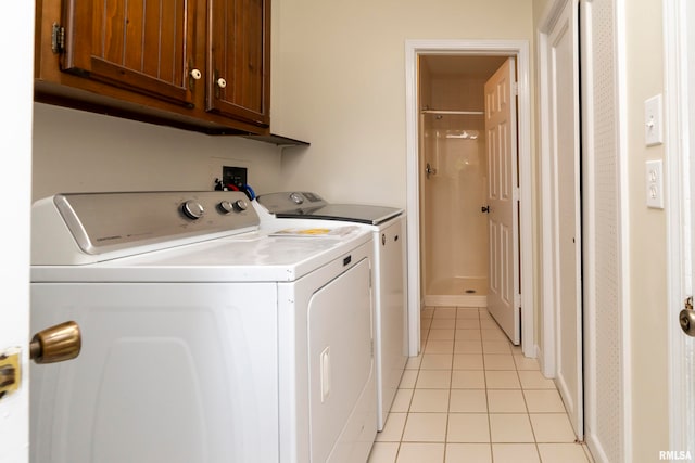 clothes washing area featuring separate washer and dryer, cabinets, and light tile patterned floors