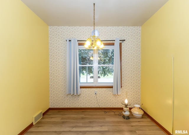 unfurnished dining area with wood-type flooring and an inviting chandelier