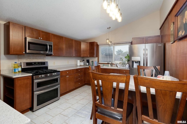 kitchen with sink, a notable chandelier, vaulted ceiling, stainless steel appliances, and decorative light fixtures