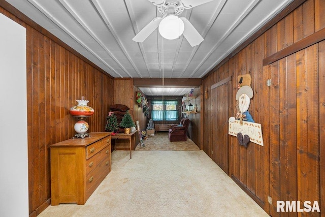 interior space with light carpet, wooden walls, and ceiling fan