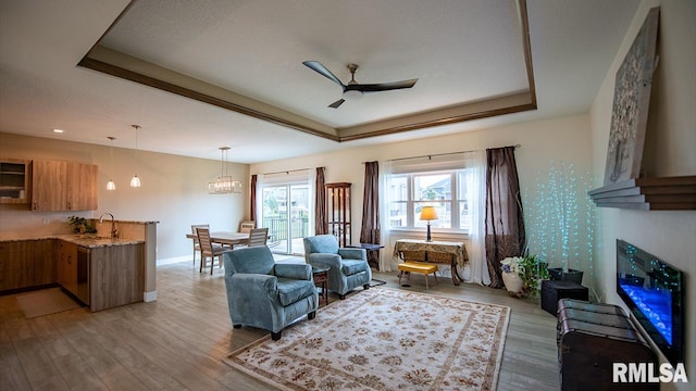 living room featuring ceiling fan with notable chandelier, a raised ceiling, a textured ceiling, wood-type flooring, and sink