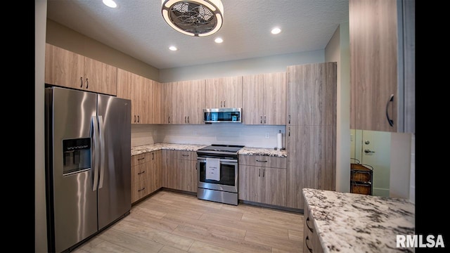 kitchen featuring light stone counters, a textured ceiling, appliances with stainless steel finishes, and light wood-type flooring