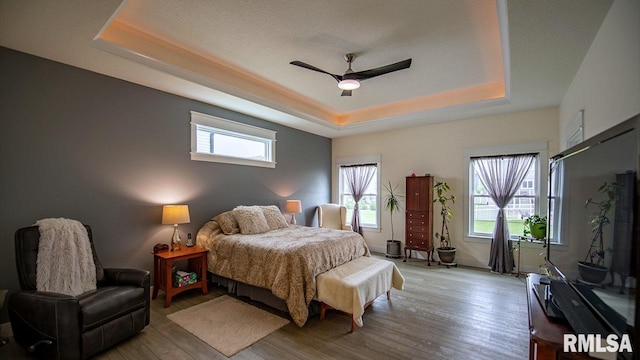 bedroom with light hardwood / wood-style flooring, ceiling fan, and a raised ceiling