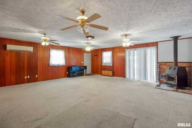 unfurnished living room with carpet floors, a wall unit AC, ceiling fan, and a wood stove