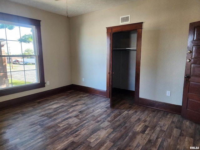 unfurnished bedroom with a textured ceiling, dark hardwood / wood-style flooring, and a closet