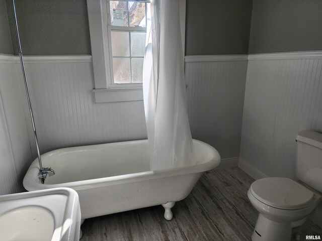 bathroom with a tub to relax in, hardwood / wood-style flooring, and toilet