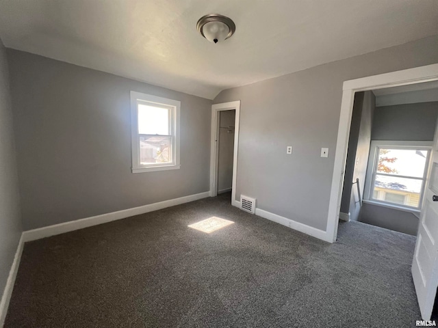 unfurnished bedroom featuring multiple windows, vaulted ceiling, dark colored carpet, and a closet