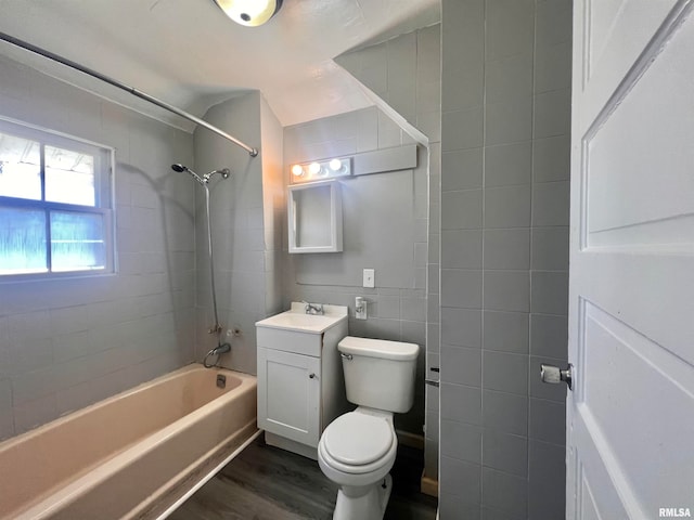 full bathroom featuring tile walls, wood-type flooring, tiled shower / bath, vanity, and toilet