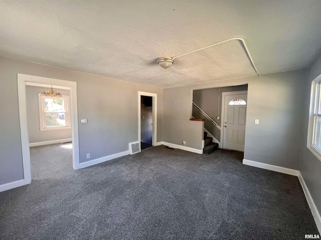 interior space featuring a textured ceiling, an inviting chandelier, and dark carpet