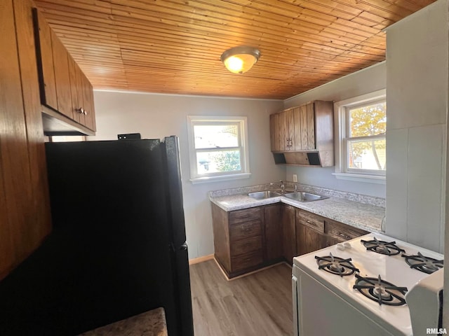 kitchen featuring wood ceiling, light hardwood / wood-style floors, white gas range oven, sink, and black refrigerator