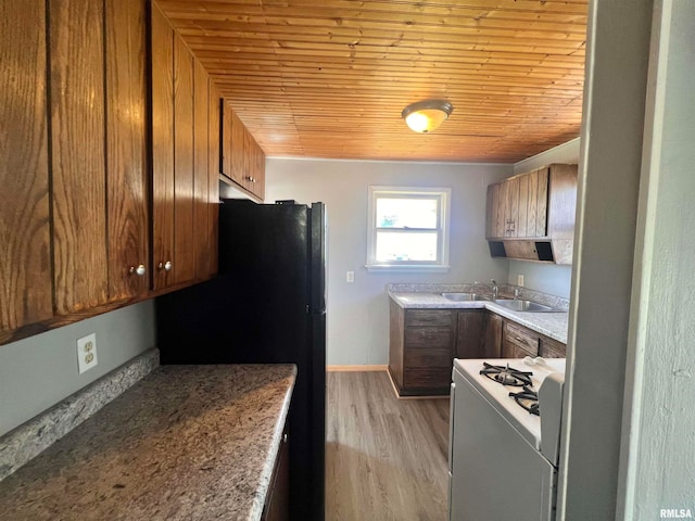 kitchen featuring light hardwood / wood-style floors, light stone counters, black refrigerator, white gas stove, and sink