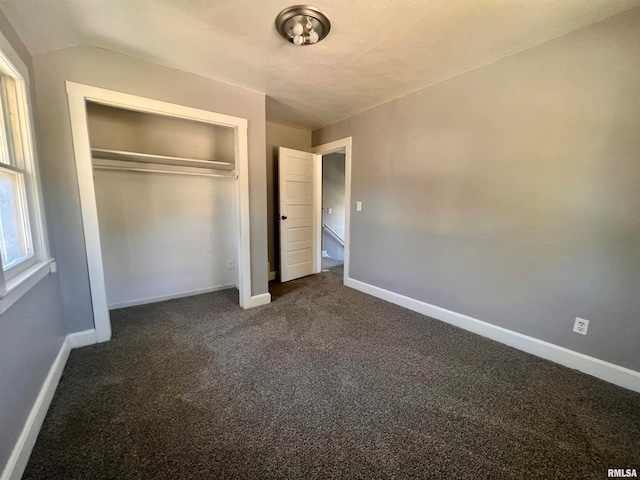 unfurnished bedroom with vaulted ceiling, dark carpet, and a closet