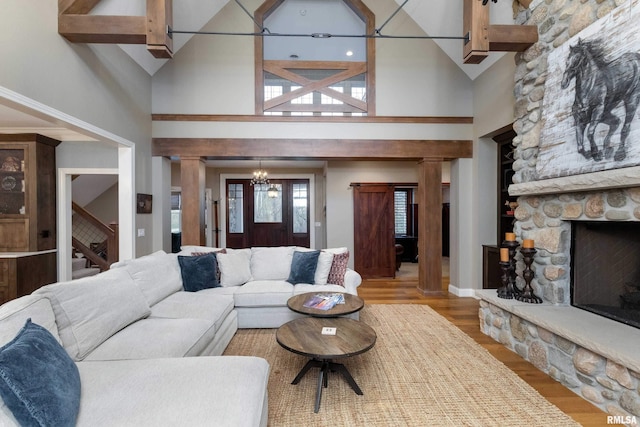 living room featuring a stone fireplace, beamed ceiling, light hardwood / wood-style flooring, a chandelier, and high vaulted ceiling