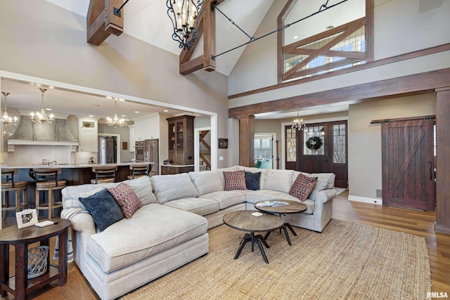 living room with light hardwood / wood-style flooring, a barn door, a chandelier, and high vaulted ceiling