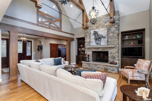 living room with a chandelier, high vaulted ceiling, beamed ceiling, a stone fireplace, and light hardwood / wood-style floors