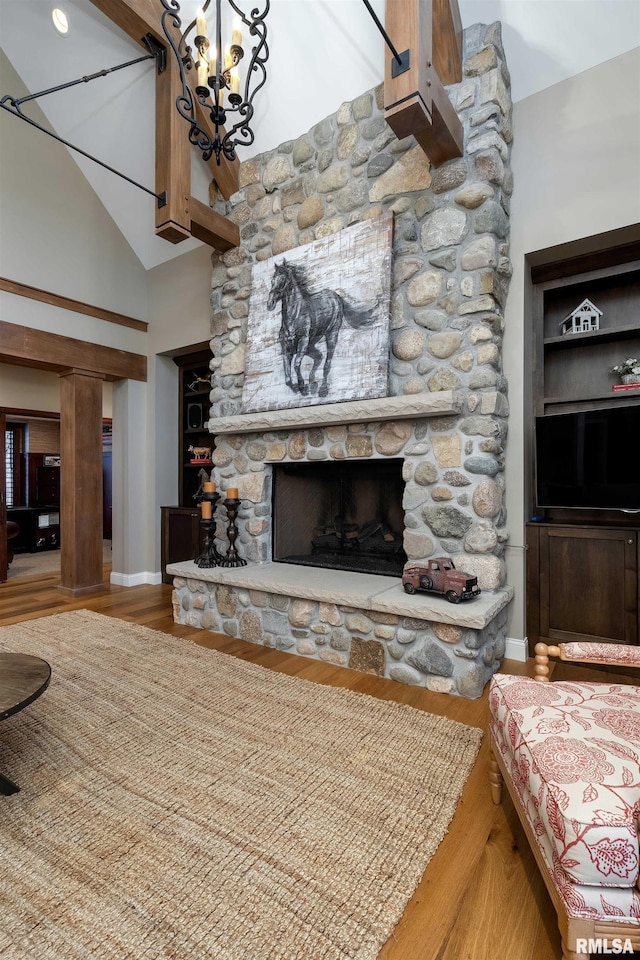 living room with hardwood / wood-style flooring, a stone fireplace, a high ceiling, and a chandelier