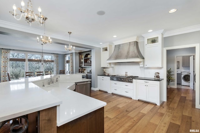 kitchen featuring custom exhaust hood, washer / clothes dryer, hanging light fixtures, a notable chandelier, and sink