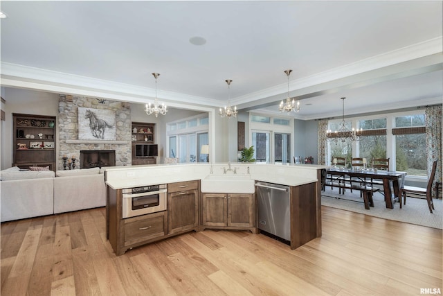 kitchen featuring a kitchen island with sink, light hardwood / wood-style flooring, stainless steel appliances, sink, and decorative light fixtures