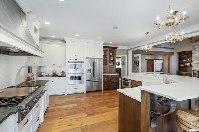 kitchen with light hardwood / wood-style flooring, hanging light fixtures, a notable chandelier, custom exhaust hood, and appliances with stainless steel finishes