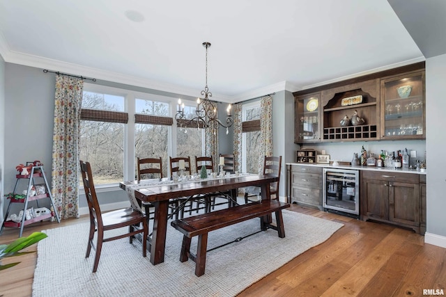 dining room with light hardwood / wood-style floors, indoor bar, wine cooler, ornamental molding, and an inviting chandelier