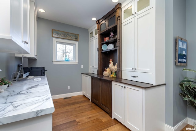 kitchen with white cabinetry, light hardwood / wood-style floors, and dark stone counters