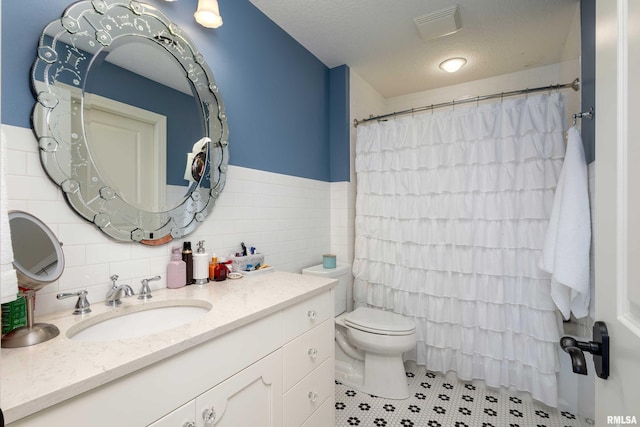 bathroom featuring tile patterned floors, toilet, vanity, tile walls, and a textured ceiling