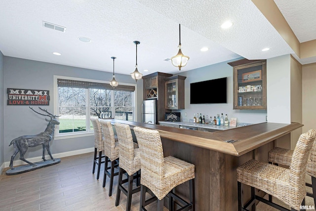 bar featuring hardwood / wood-style floors, hanging light fixtures, a textured ceiling, and stainless steel refrigerator