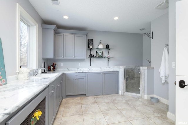 kitchen with sink, light stone countertops, light tile patterned floors, gray cabinets, and a textured ceiling