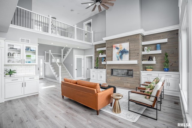 living room with ceiling fan, a towering ceiling, and light wood-type flooring