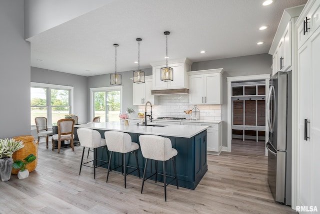 kitchen featuring stainless steel appliances, pendant lighting, a center island with sink, white cabinets, and light hardwood / wood-style floors