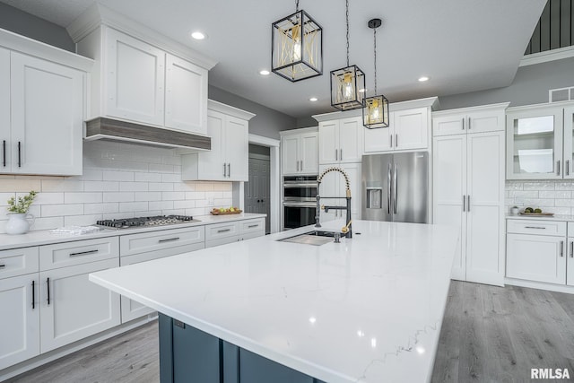 kitchen featuring tasteful backsplash, stainless steel appliances, a kitchen island with sink, decorative light fixtures, and white cabinetry