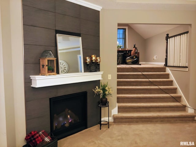 stairs with a large fireplace, vaulted ceiling, and carpet