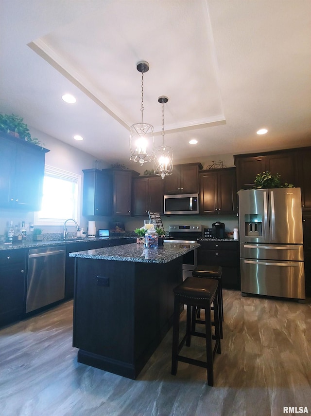 kitchen with hanging light fixtures, stainless steel appliances, dark stone counters, a tray ceiling, and a kitchen island