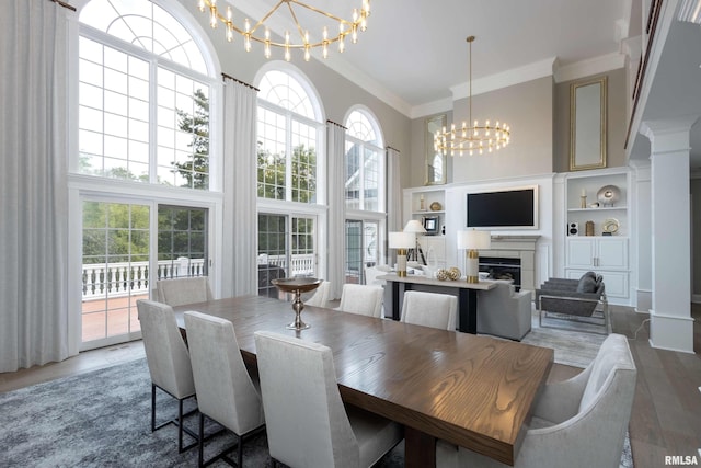 dining room featuring a chandelier, a tile fireplace, a towering ceiling, hardwood / wood-style floors, and crown molding