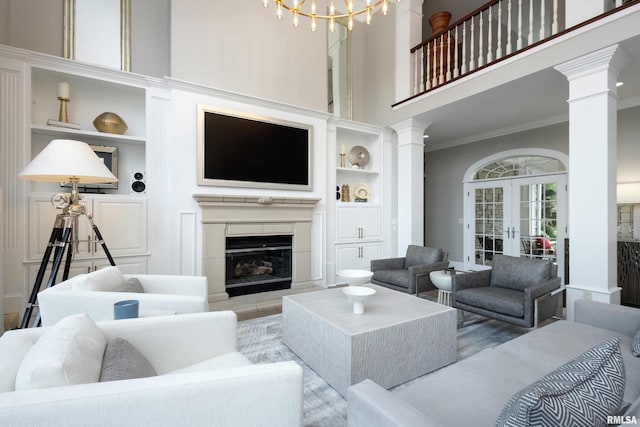 living room featuring a fireplace, a towering ceiling, crown molding, french doors, and built in features