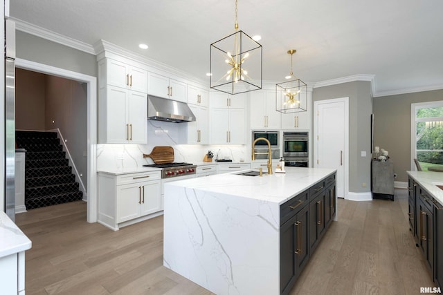 kitchen with white cabinets, a kitchen island with sink, decorative light fixtures, stainless steel appliances, and light wood-type flooring