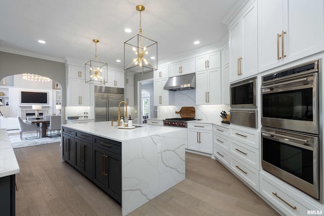 kitchen with pendant lighting, built in appliances, a center island with sink, and white cabinetry