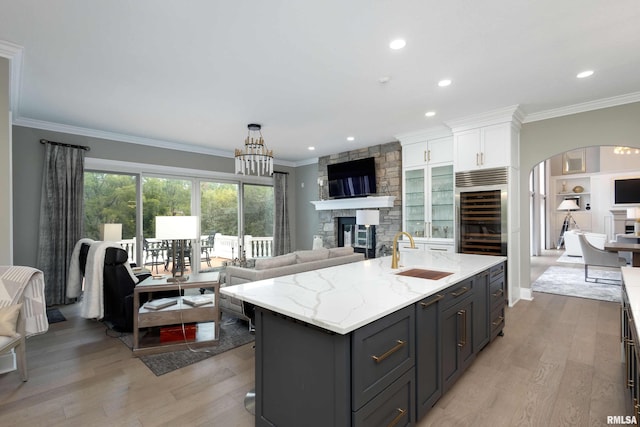 kitchen with sink, a center island with sink, white cabinetry, a fireplace, and light hardwood / wood-style floors