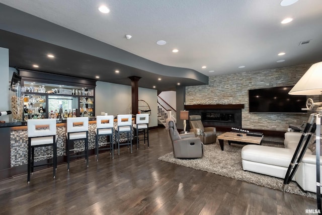 living room with a textured ceiling, dark hardwood / wood-style floors, a fireplace, indoor bar, and ornate columns