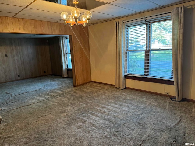 carpeted empty room featuring wood walls, a paneled ceiling, and a chandelier