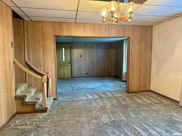 carpeted empty room featuring wood walls, a chandelier, and a paneled ceiling