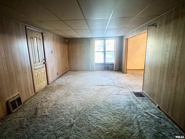 carpeted empty room featuring wooden walls and visible vents