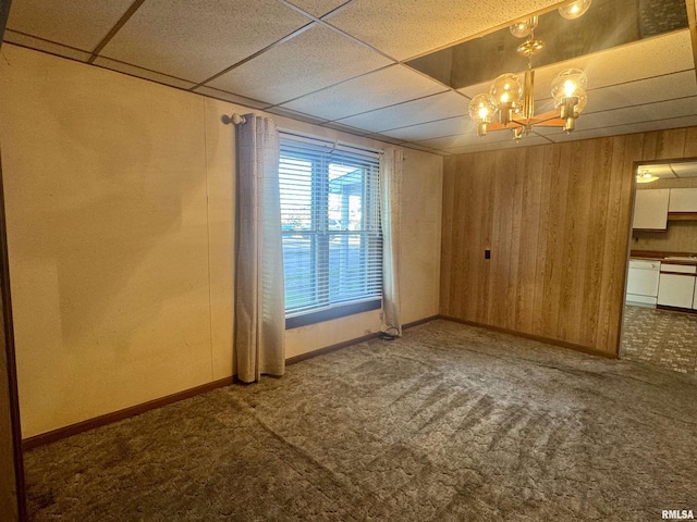 carpeted spare room featuring wooden walls, baseboards, a notable chandelier, and a paneled ceiling