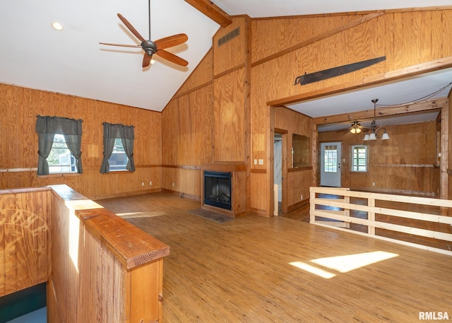 unfurnished living room featuring wood-type flooring, wooden walls, beam ceiling, and high vaulted ceiling