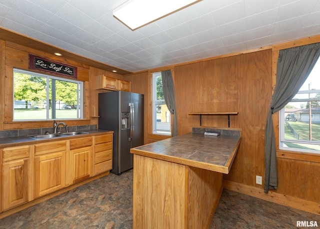 kitchen featuring wooden walls, stainless steel refrigerator with ice dispenser, kitchen peninsula, and sink