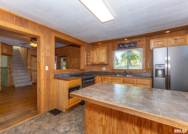 kitchen with wood walls, sink, dark wood-type flooring, stainless steel refrigerator with ice dispenser, and tile counters