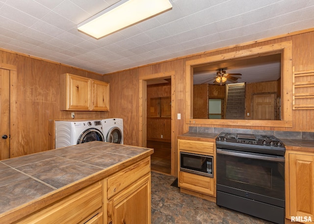 kitchen featuring wood walls, black range with electric cooktop, washing machine and clothes dryer, and tile countertops