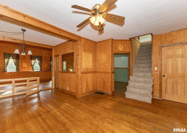 unfurnished living room with ceiling fan with notable chandelier, wood-type flooring, and wooden walls